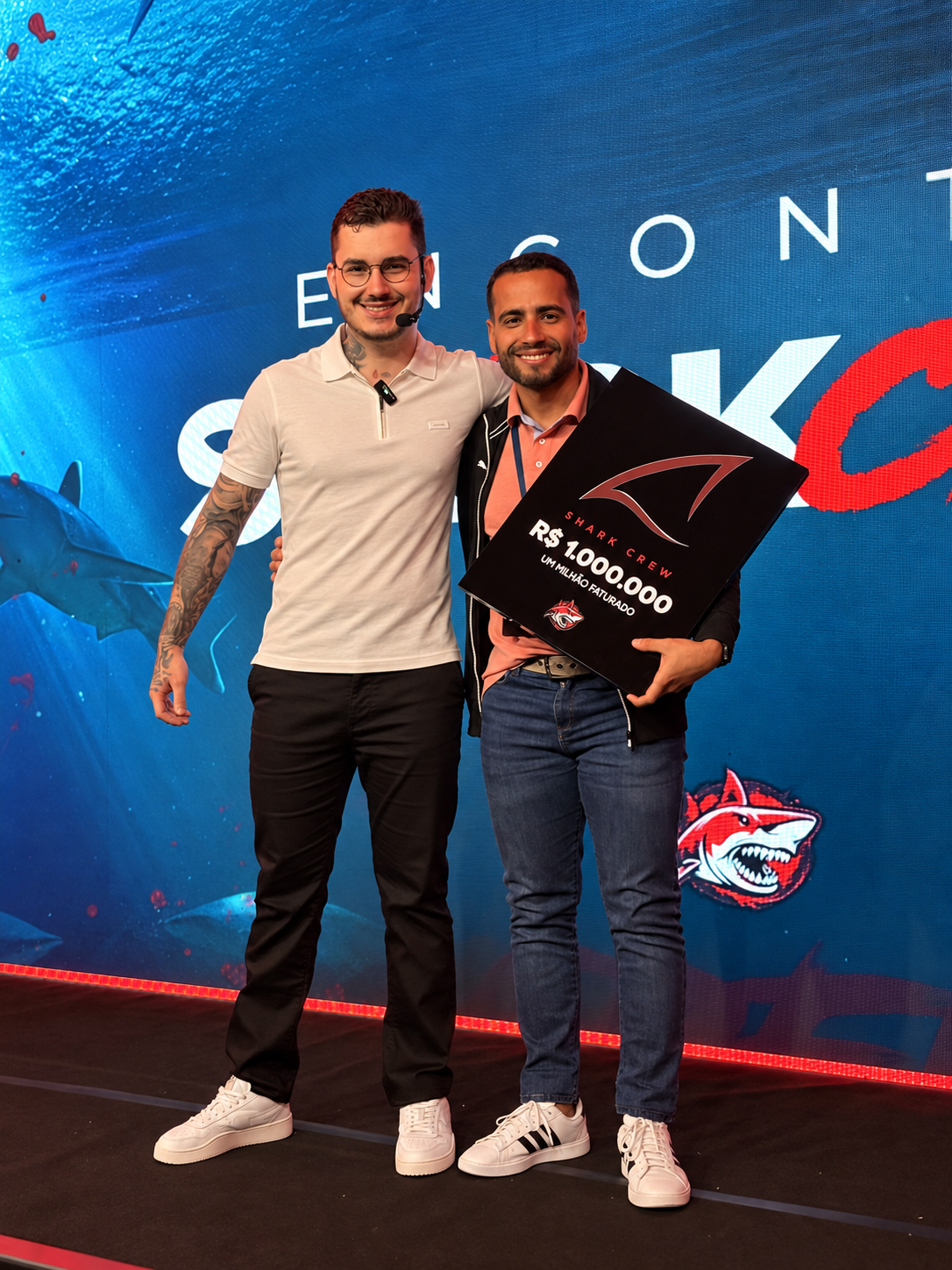 Victor e Thiago no palco segurando a placa Shark Crew de R$ 1.000.000 faturado